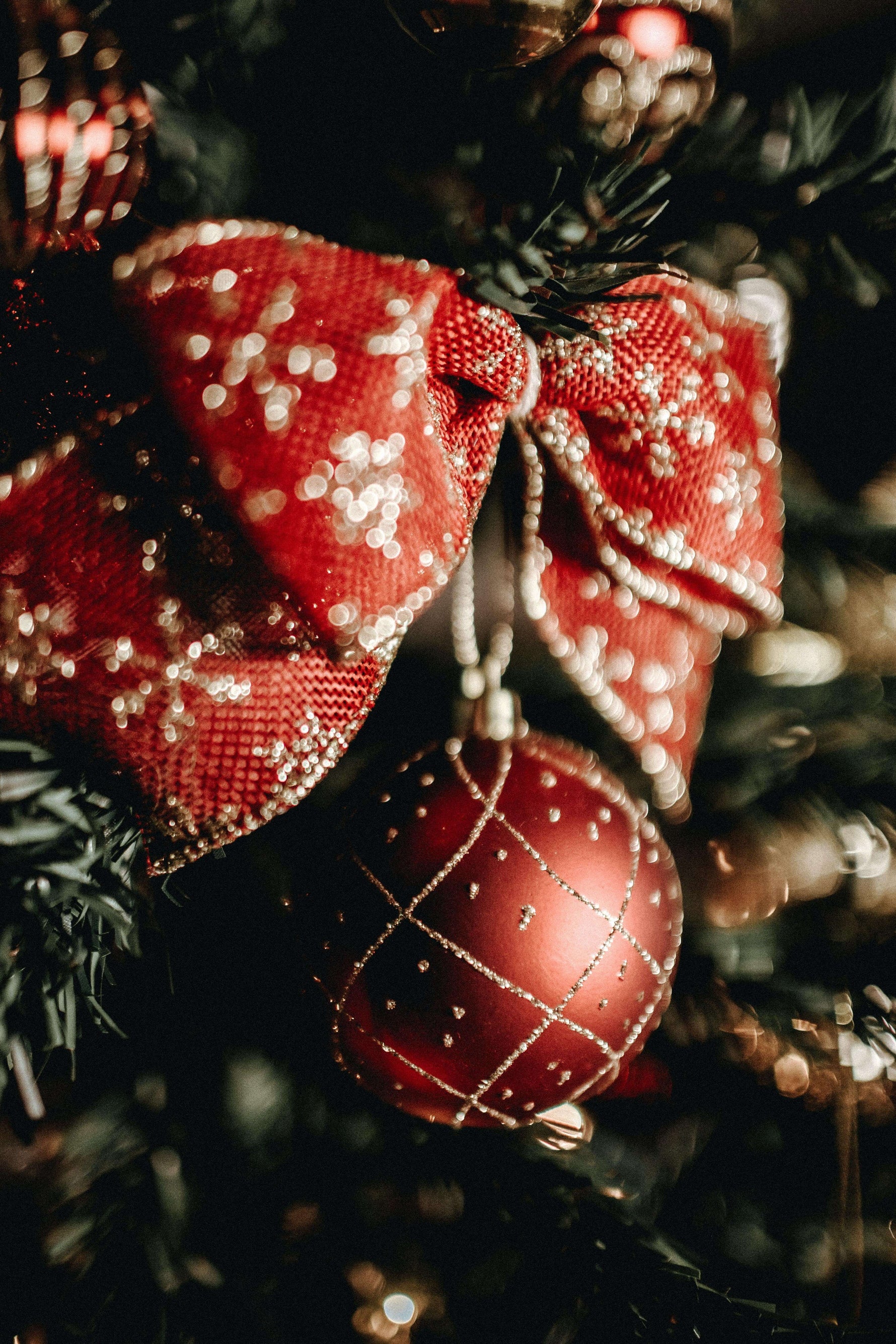 A close-up view of a red and white Christmas ornament and bow hanging on a tree
