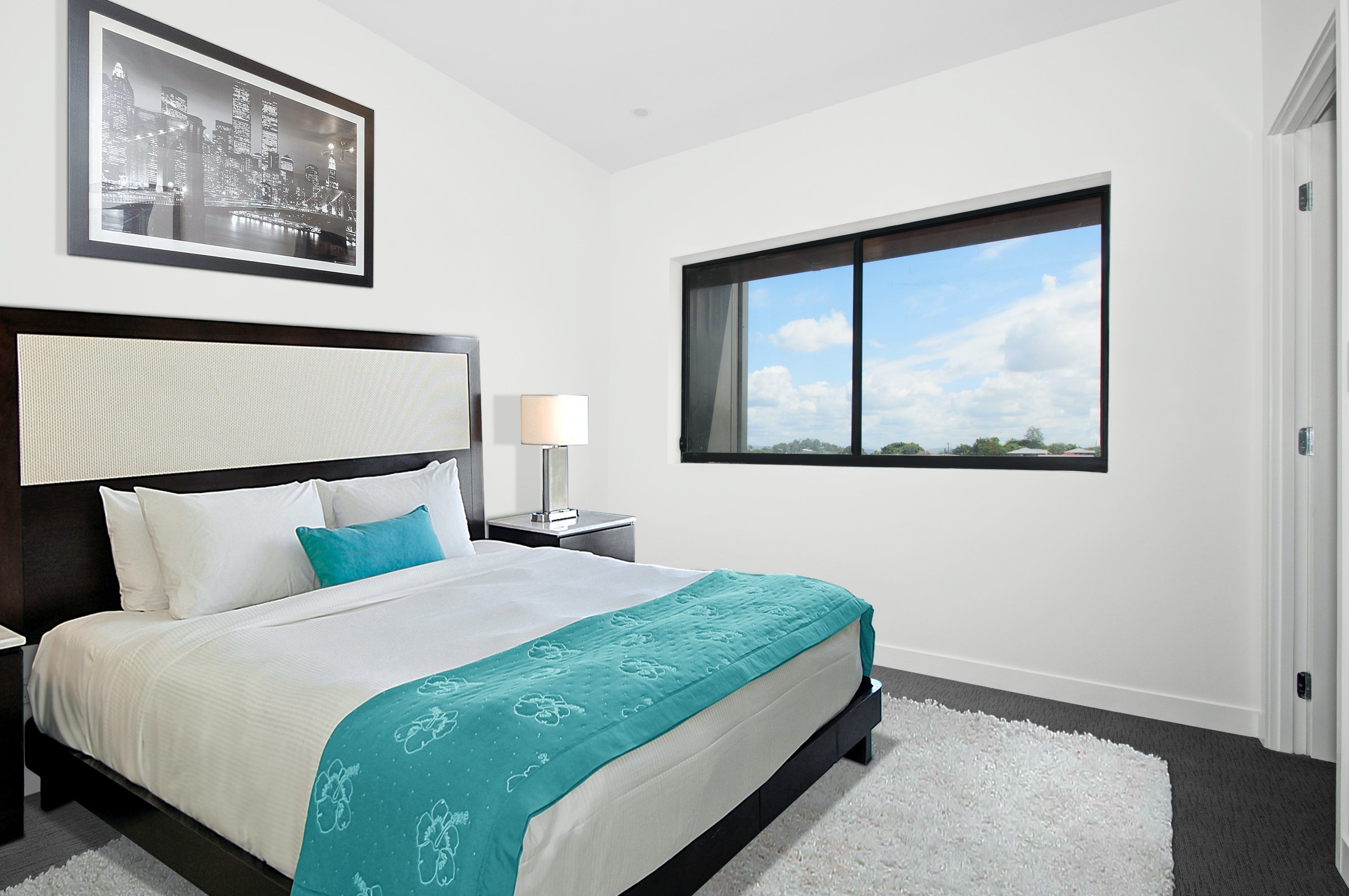hotel bed with luxury white sheets and pillows, blue duvet, picture, window, and lamp