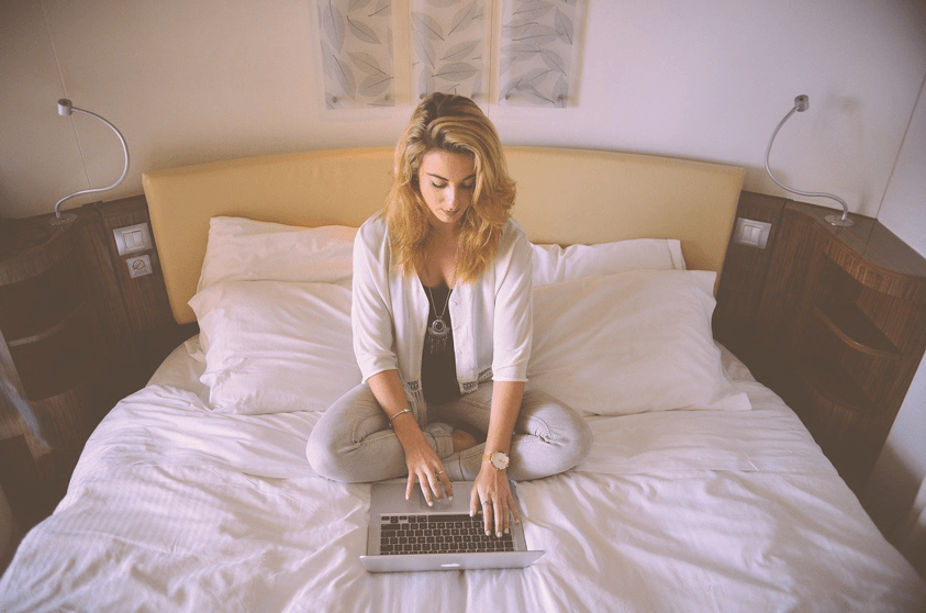 Woman Sitting on Bed and Typing on Laptop